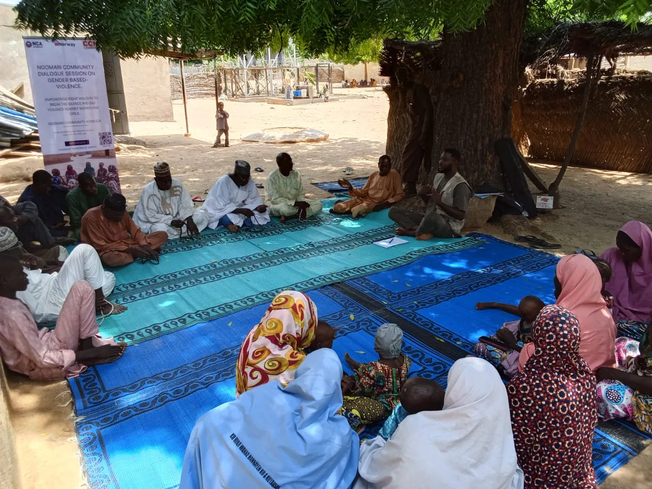 Participants seated on a mat beneath a tree